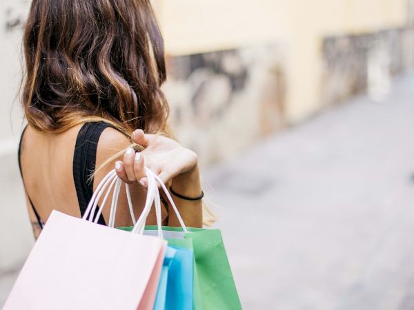 A person walking away with several colorful shopping bags, stylish summer outfit, and a street scene in the background, inviting shopping vibes.
