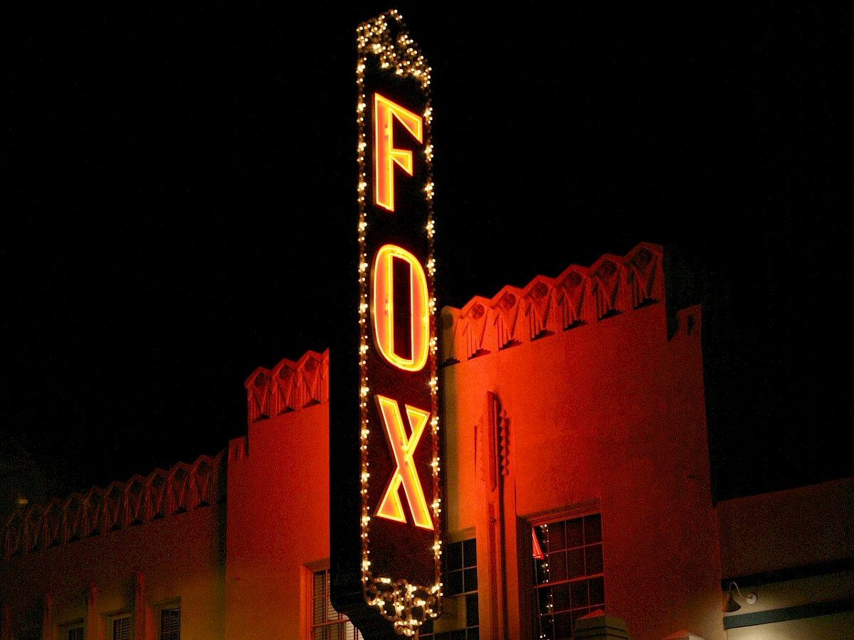 A neon Fox Theatre sign glows above a closed marquee outside, advertising a sold-out show on a dimly lit street, nighttime ambiance. End.