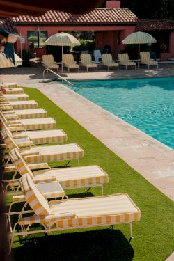 Rows of yellow-striped lounge chairs by a turquoise pool, with umbrellas and a pink building in the background. end.